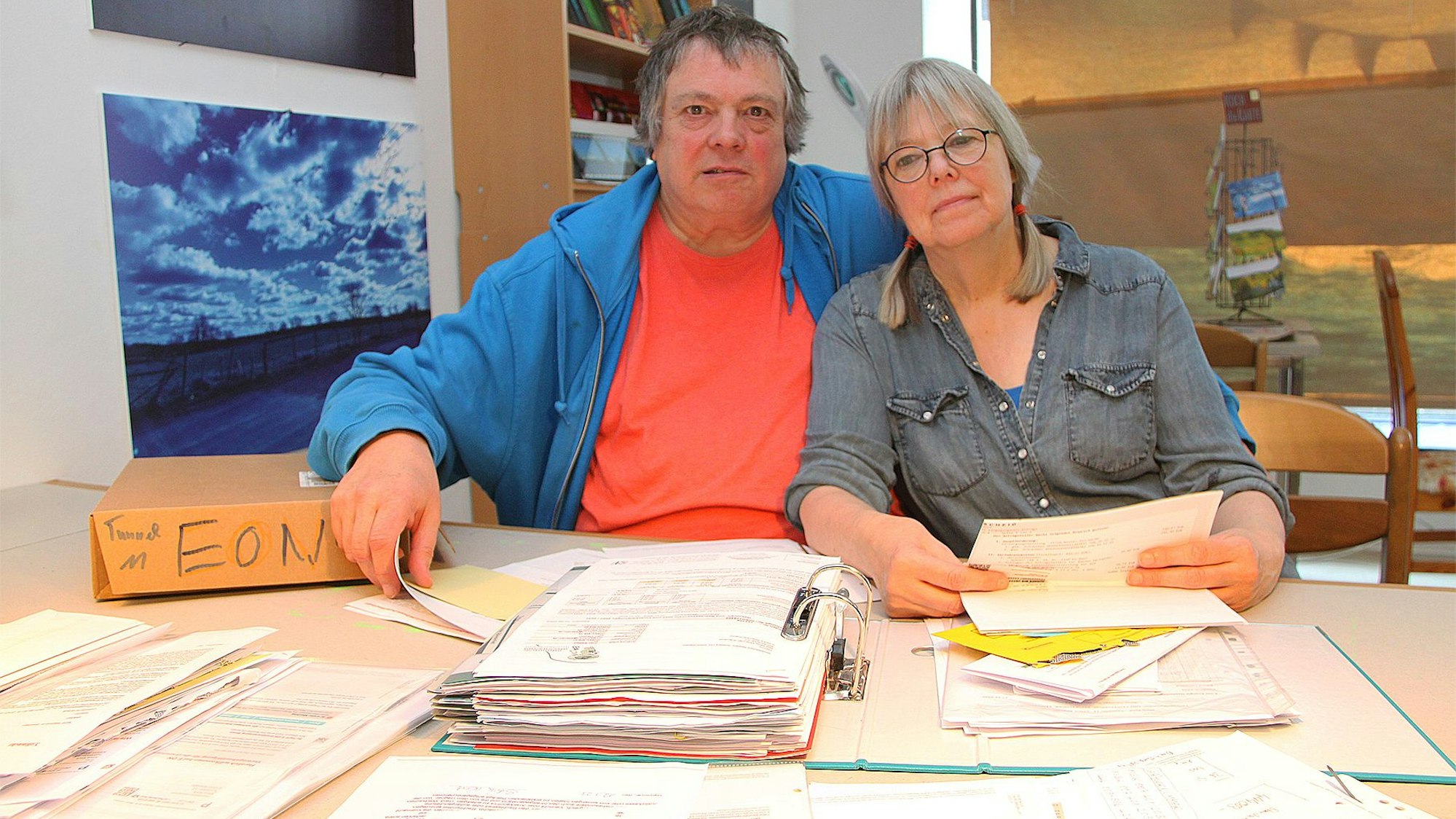 Hartwig Kausch und Silvia Kock sitzen an einem Tisch. Vor ihnen liegen Aktenordner und Papierstapel.