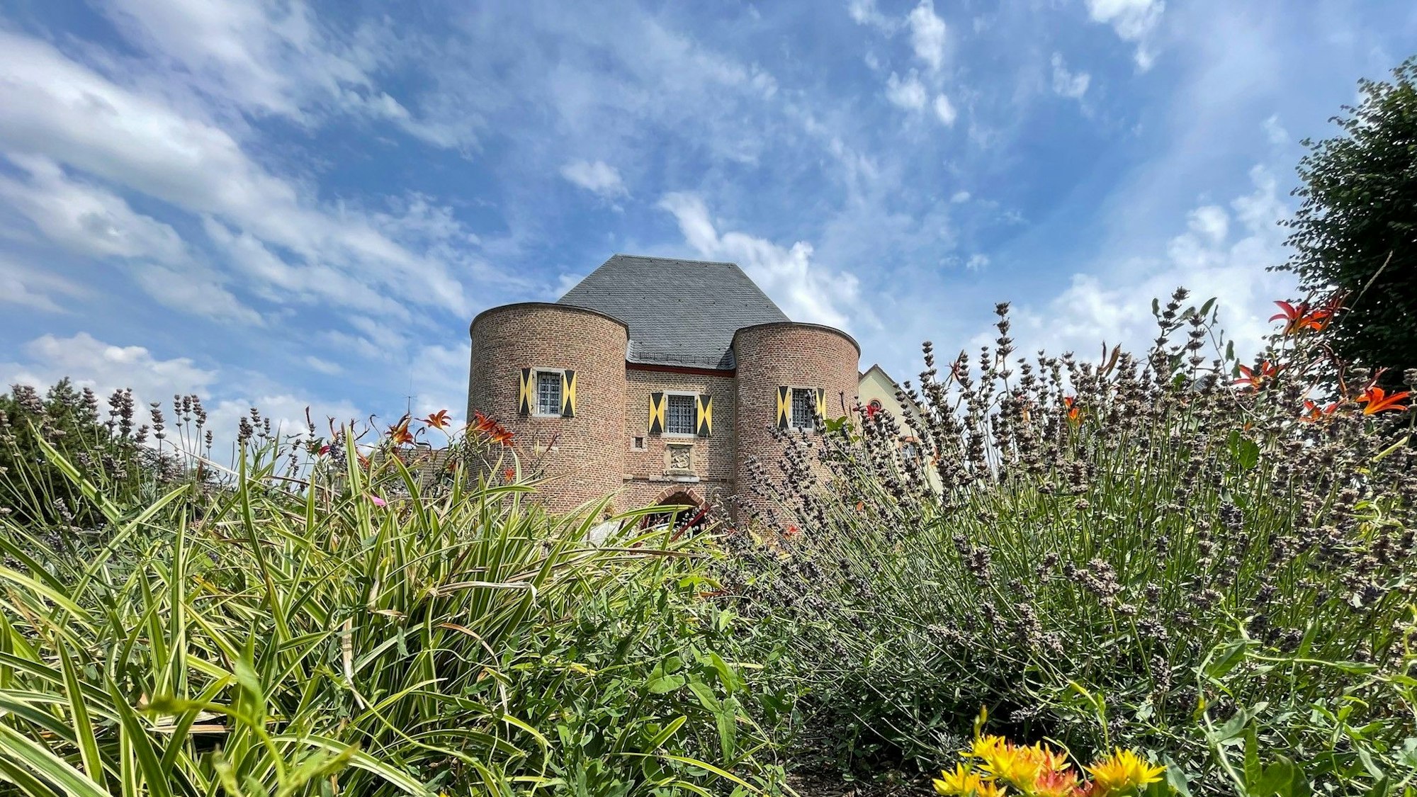 Das Aachener Tor in Bergheim vor blauem Himmel. Im Vordergrund eine blühende Wiese.