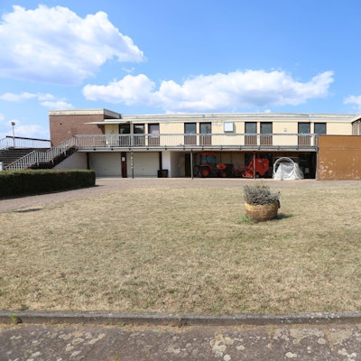 Die Rückseite der Sporthalle Menzenberg mit in die Jahre gekommenen Bauten. Im Vordergrund steht ein Blumenkübel.
