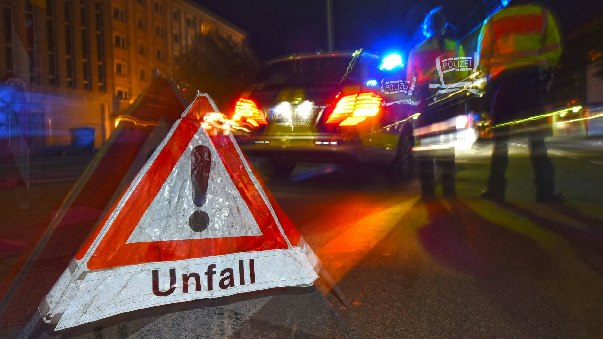 Ein Polizeifahrzeug steht mit Blaulicht auf der Straße. Daneben steht ein Warndreieck mit dem Schriftzug «Unfall».