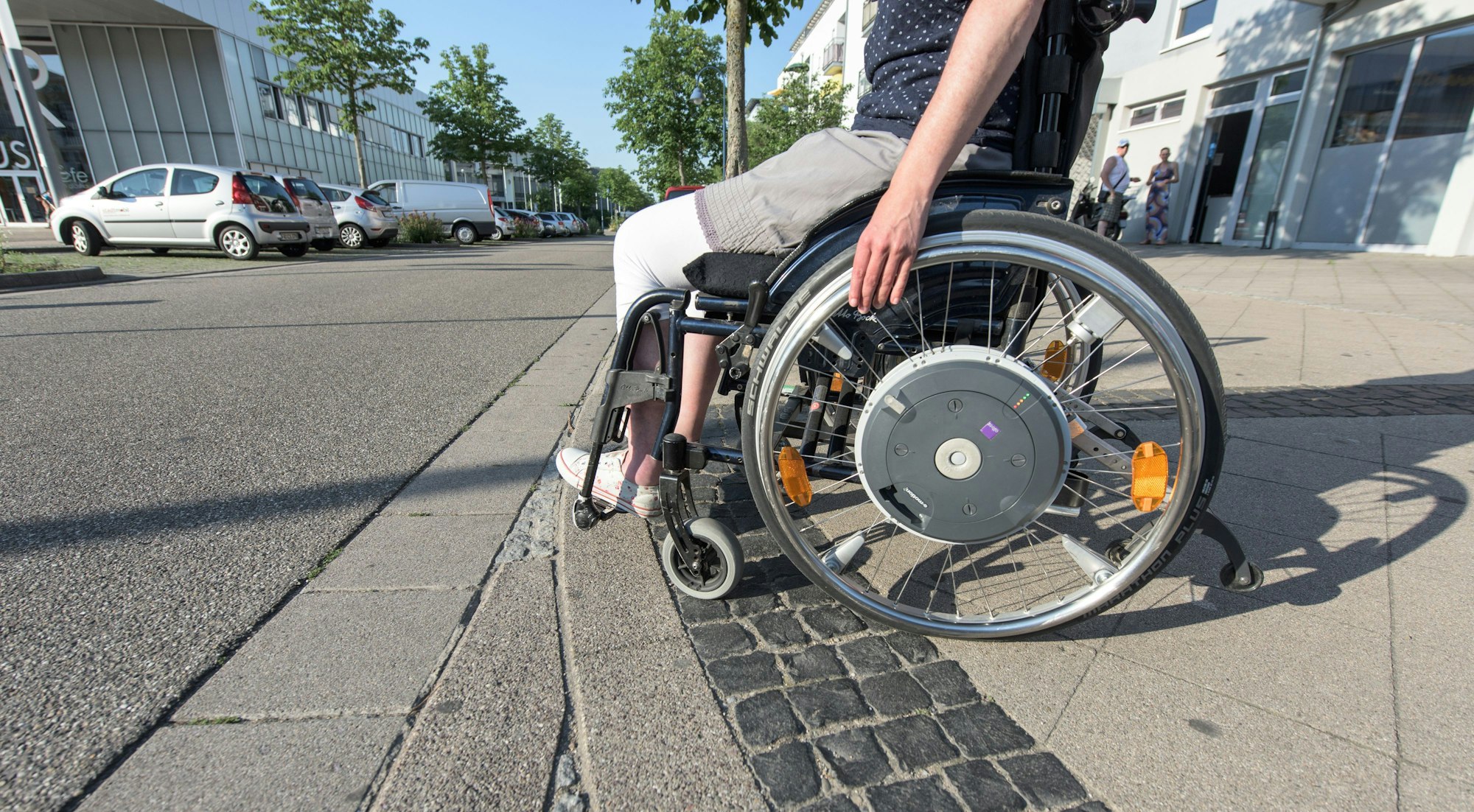 Eine Rollstuhlfahrerin steht auf einem Bürgersteig. In Kleve haben mutmaßlich vier Täter eine Rollstuhlfahrerin beklaut - wohl zum zweiten Mal innerhalb von zwei Wochen. (Symbolbild)