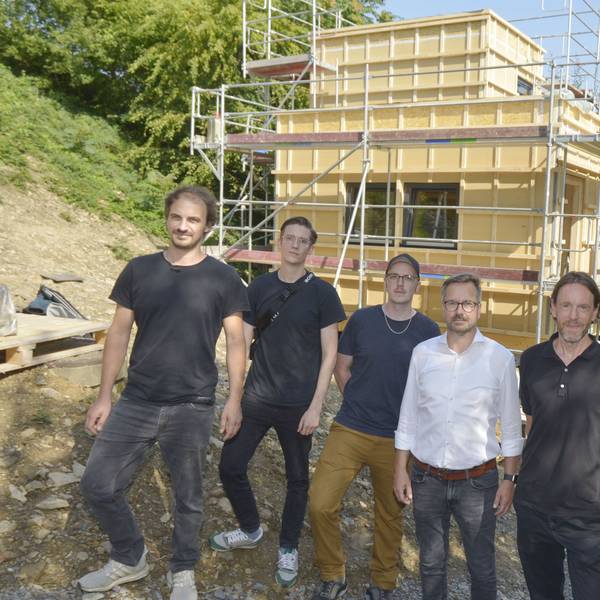 Sechs Männer stehen vor einem Häuserneubau.
