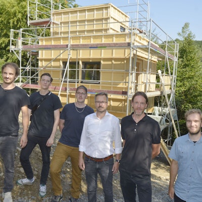 Sechs Männer stehen vor einem Häuserneubau.