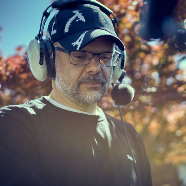 Constantin Bömers trägt ein großes Headset und eine Mütze. Er hat eine Brille und hat einen graumelierten Bart.
