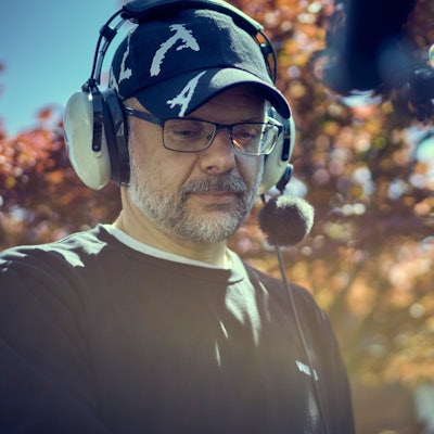 Constantin Bömers trägt ein großes Headset und eine Mütze. Er hat eine Brille und hat einen graumelierten Bart.