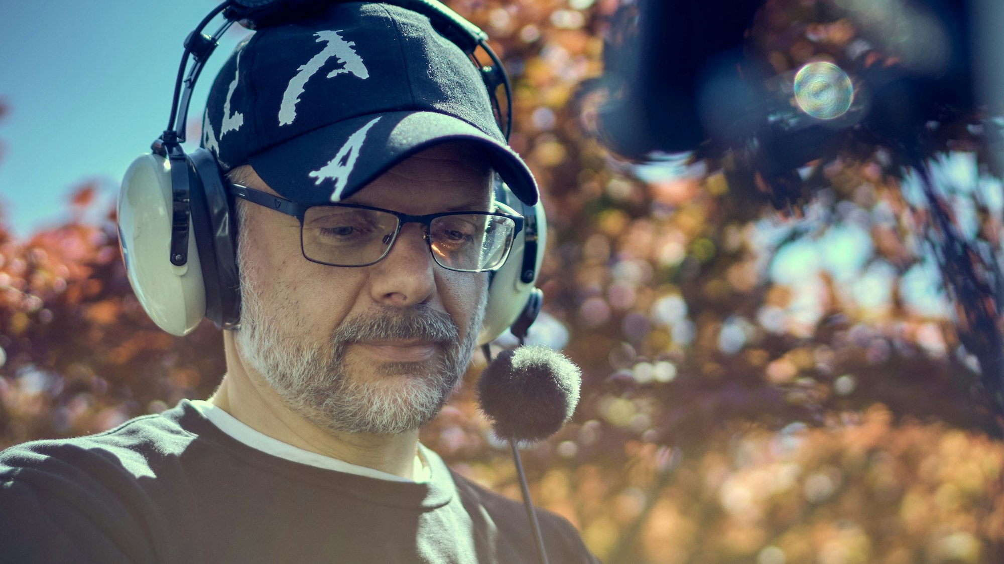 Constantin Bömers trägt ein großes Headset und eine Mütze. Er hat eine Brille und hat einen graumelierten Bart.