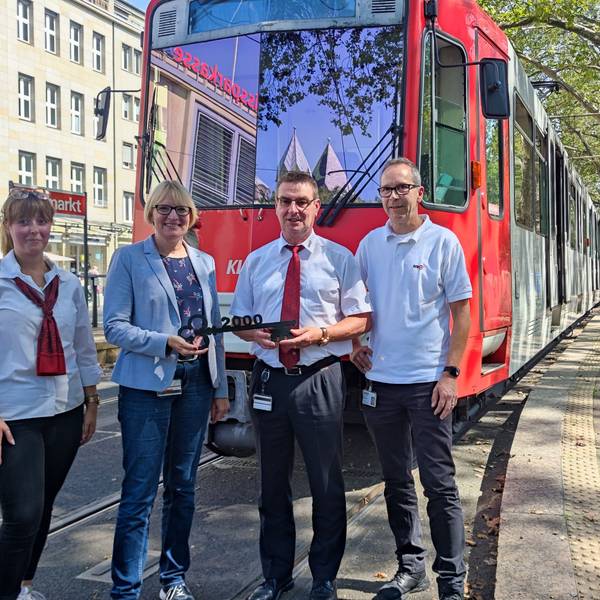 Die vier Personen stehen am Neumarkt vor einer ausrangierten Bahn. Stefanie Haaks überreicht Frank Faßbender einen Schlüssel