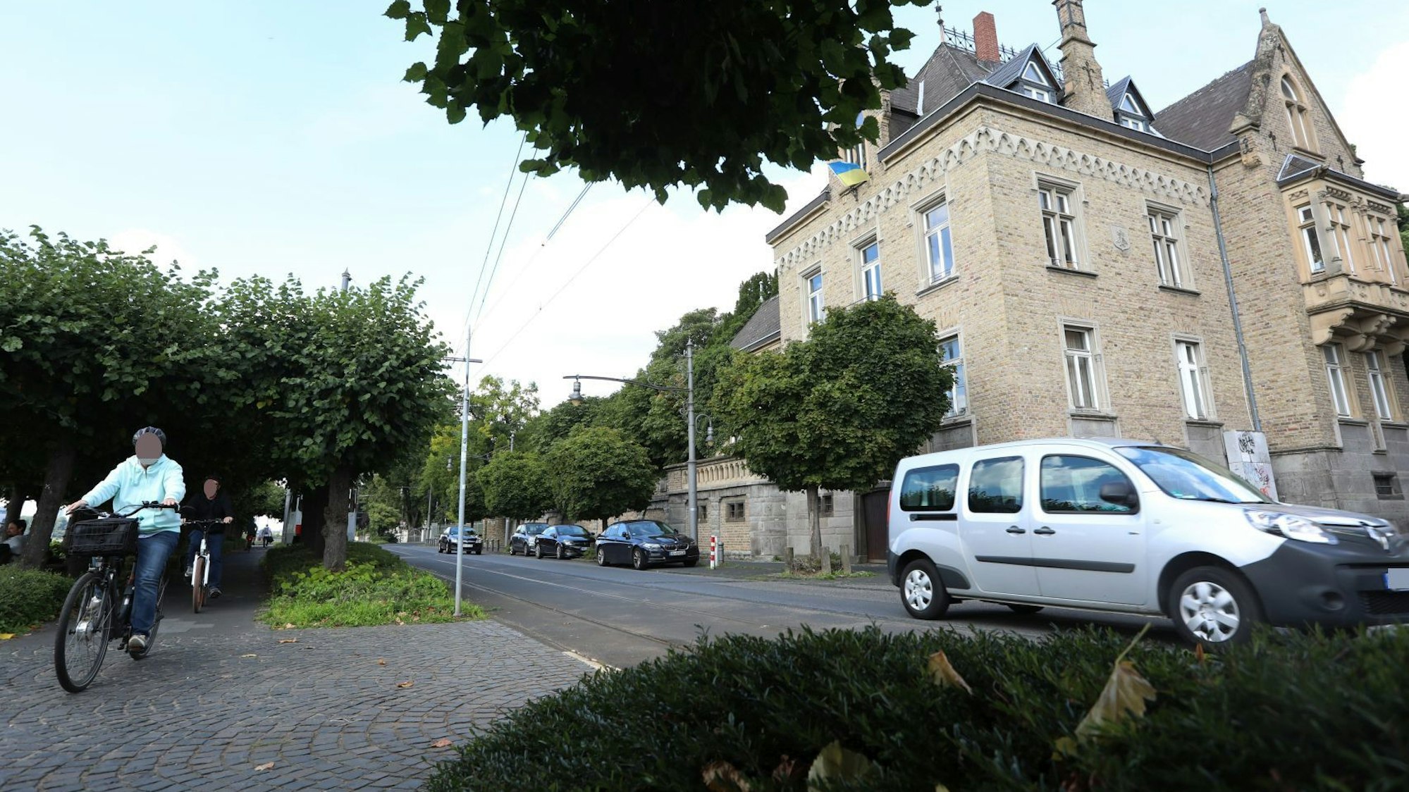 Zwei Radfahrer benutzen den Rheinradweg auf der Promenade, ein Auto fährt über die rechts davon gelegene Rheinallee.
