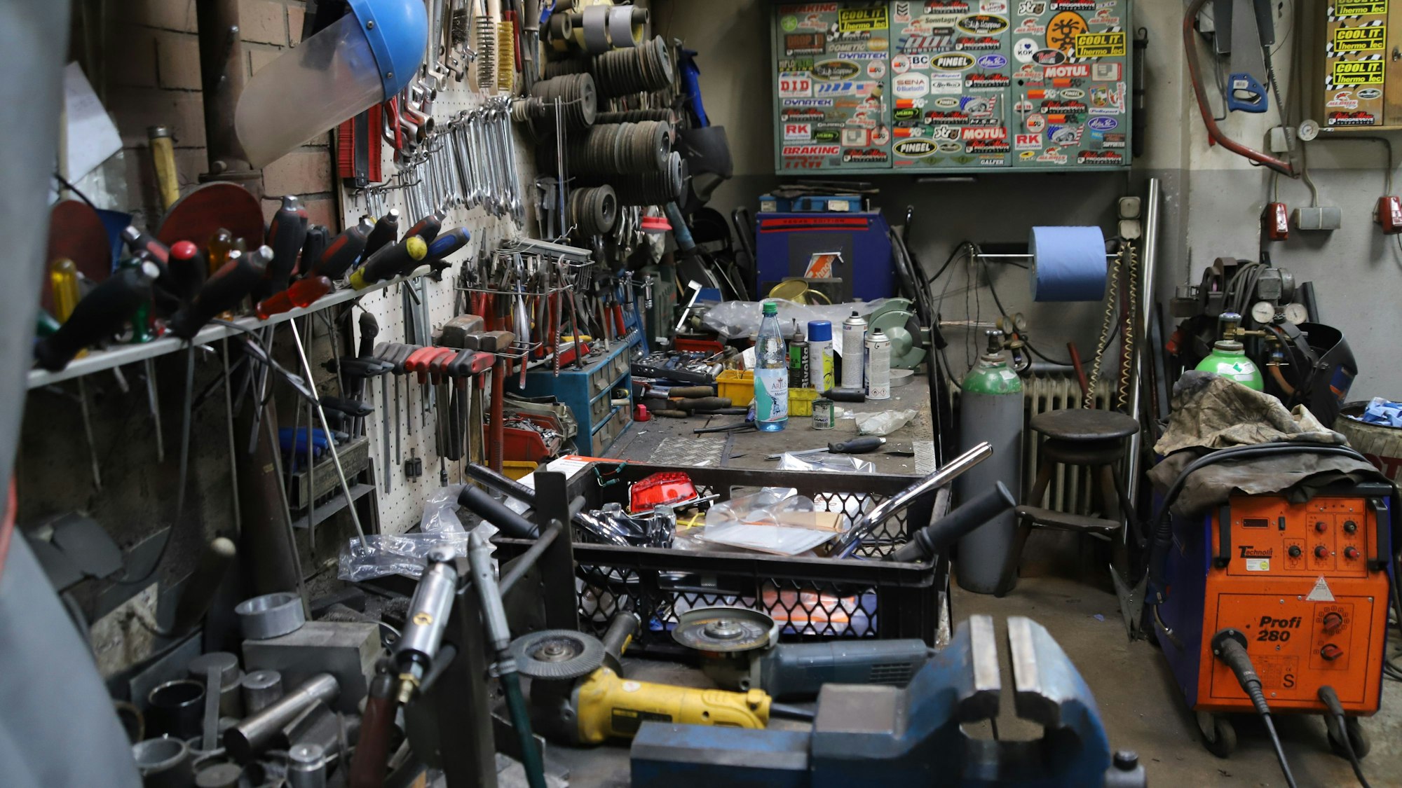 Auf engstem Raum sind Werkzeuge, Reifen und andere Ersatzteile auf, über und neben einer Werkbank angeordnet.