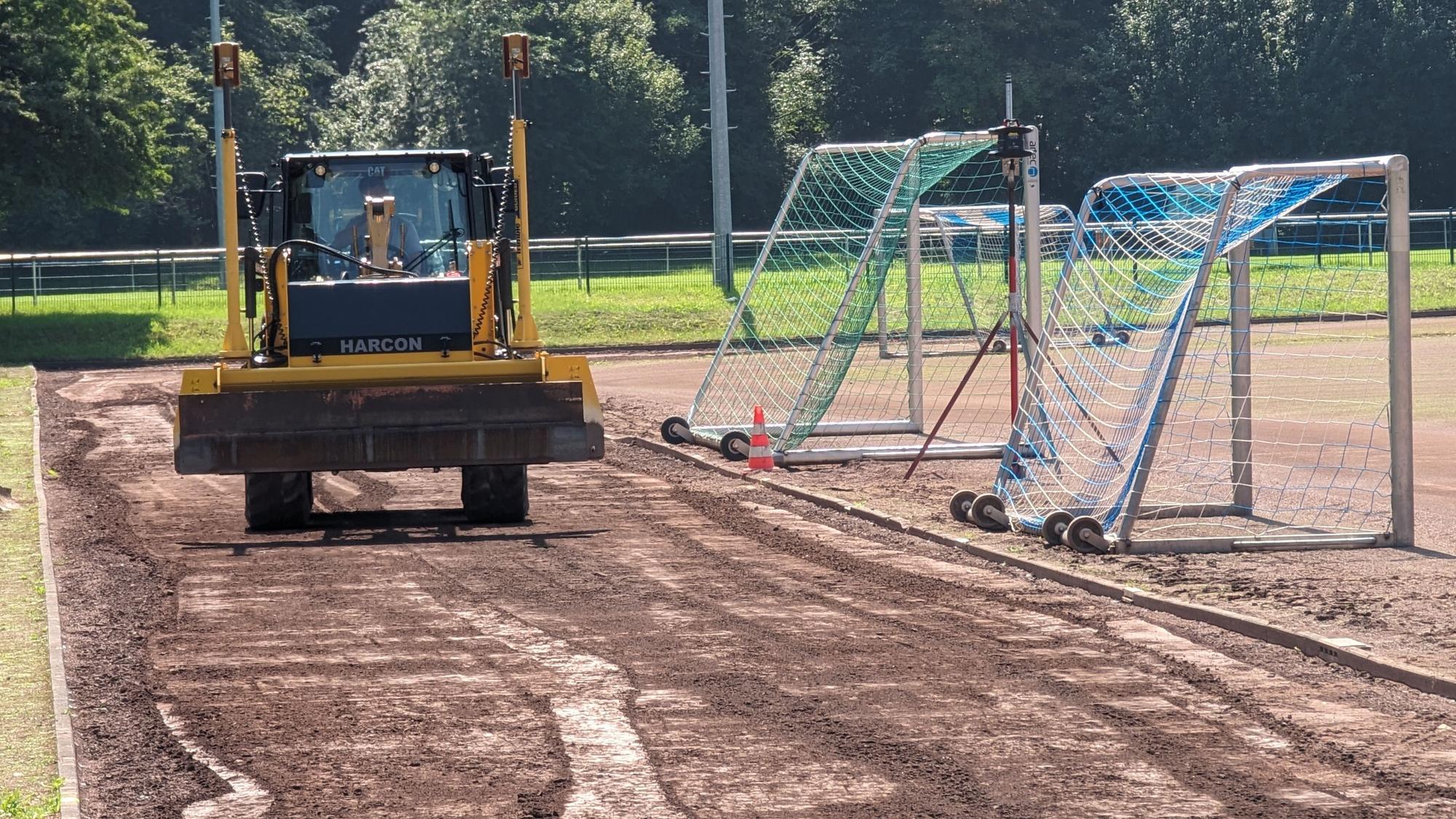 Ein Bagger schiebt den Aschenbelag auf dem Sportplatz zusammen.