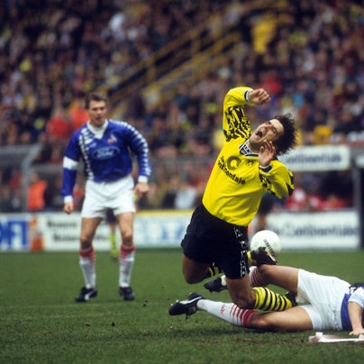 Ein Spieler des 1. FC Köln in ungewohntem blauen Trikot foult seinen Dortmunder Gegenspieler.