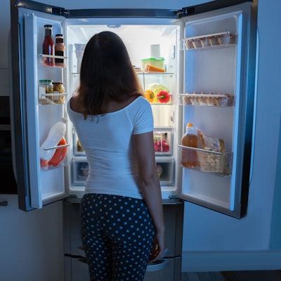 Rückansicht einer Frau, die vor einem Kühlschrank steht