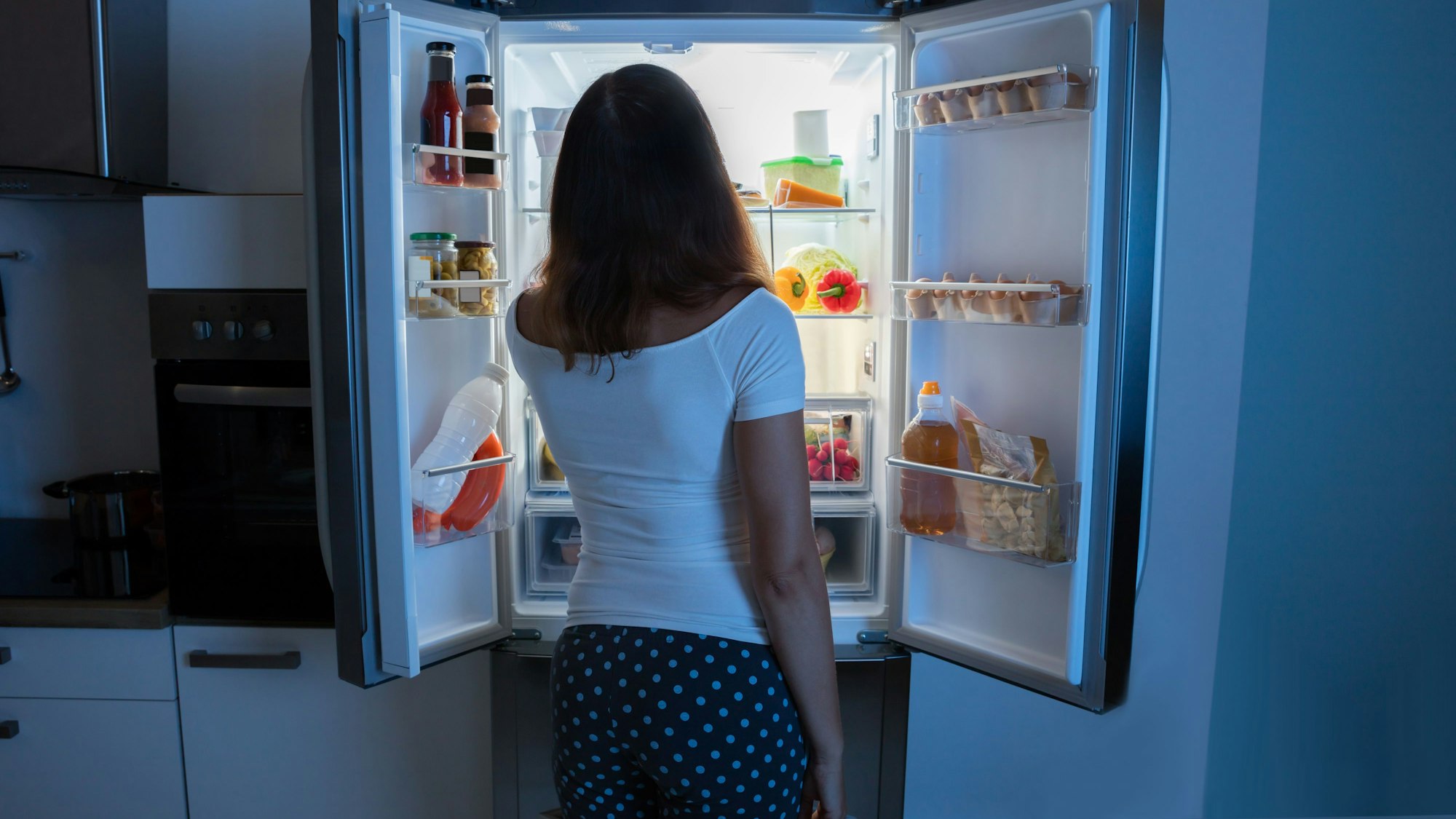 Rückansicht einer Frau, die vor einem Kühlschrank steht