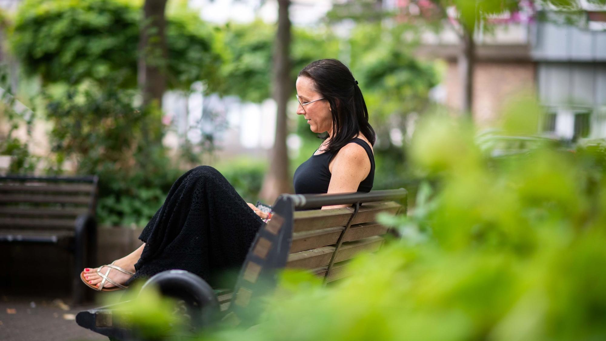 Michaela Schmidt sitzt auf einer Bank und schaut in ihr Handy.