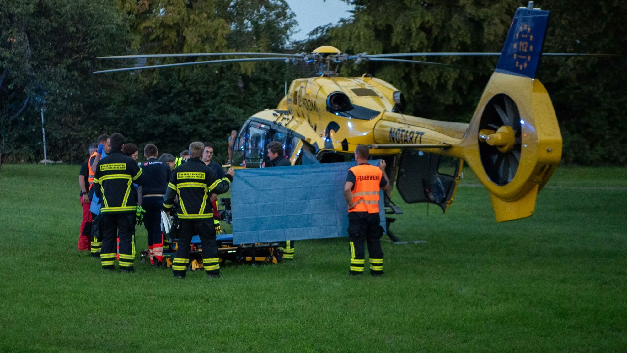 Das Bild zeigt einige Rettungskräfte vor dem Hubschrauber. Es ist ein Sichtschutz gespannt.