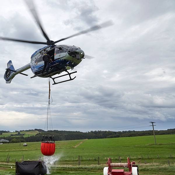 Das Bild zeigt den Polizeihubschrauber mit dem angehängten Wasserbehälter, der gerade aus einem Faltbehälter befüllt worden ist.