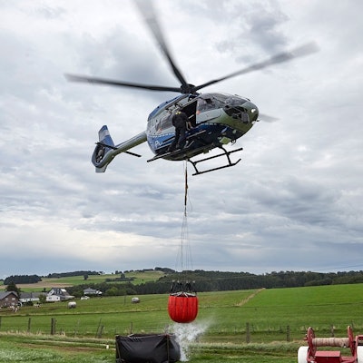Das Bild zeigt den Polizeihubschrauber mit dem angehängten Wasserbehälter, der gerade aus einem Faltbehälter befüllt worden ist.