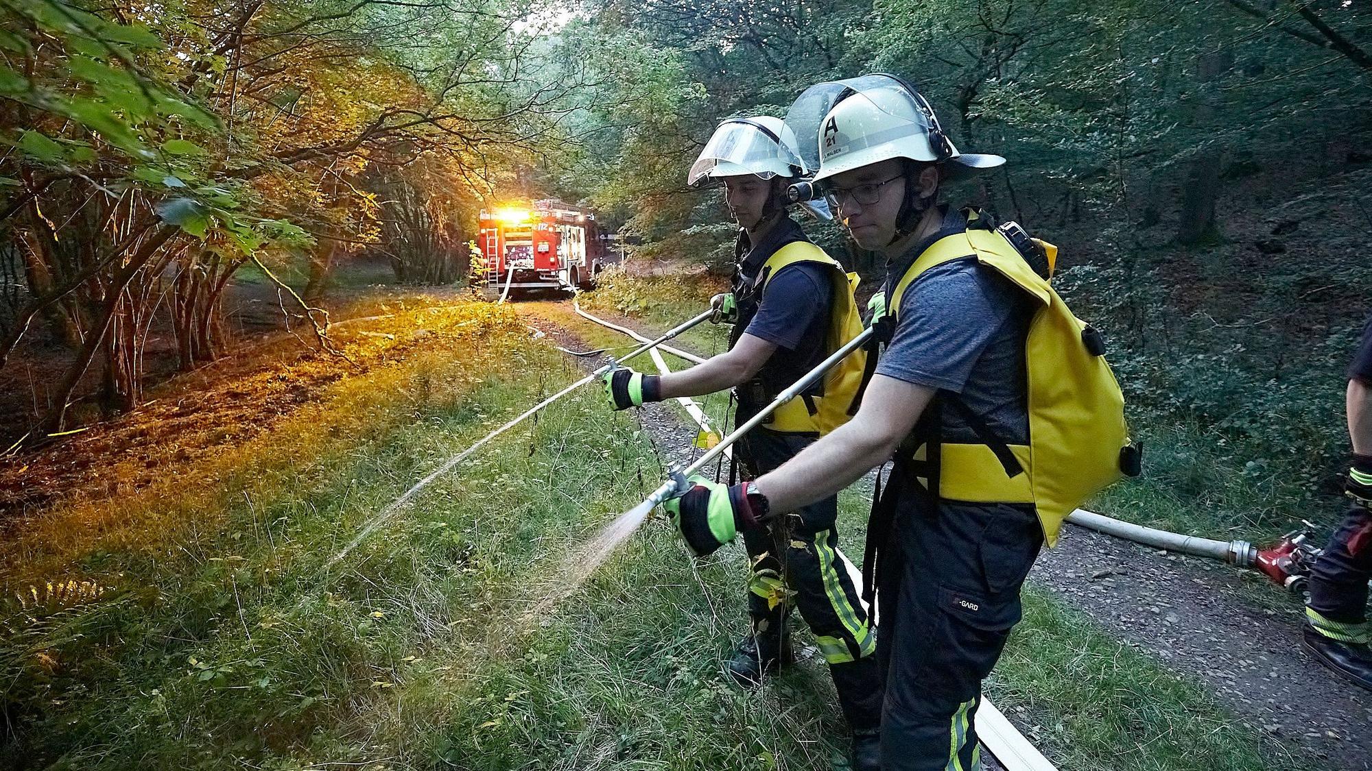 Das Bild zeigt zwei Feuerwehrmänner, die während einer Übung mithilfe ihrer Löschrucksäcke eine Wiese bewässern.