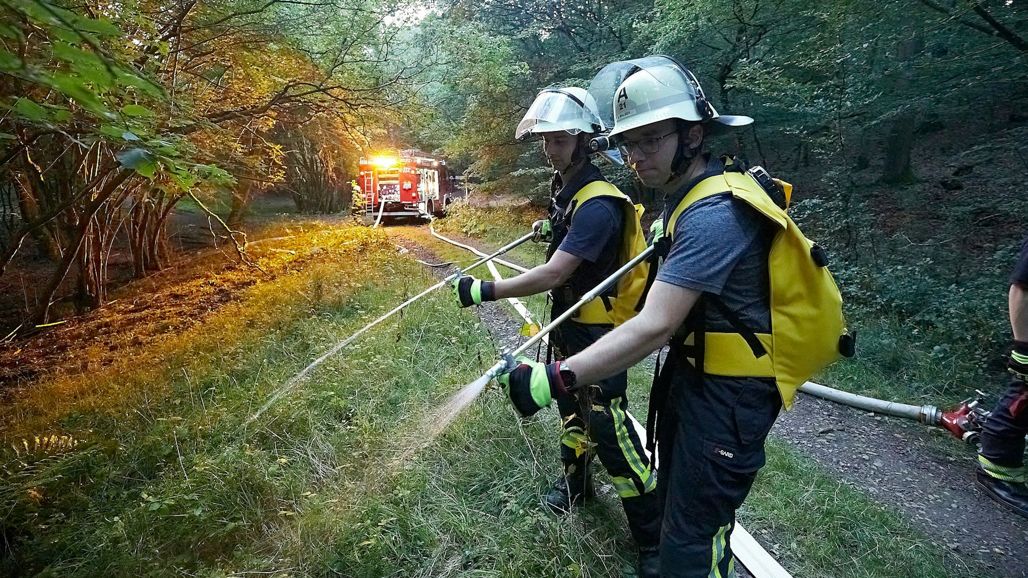 Das Bild zeigt zwei Feuerwehrmänner, die während einer Übung mithilfe ihrer Löschrucksäcke eine Wiese bewässern.