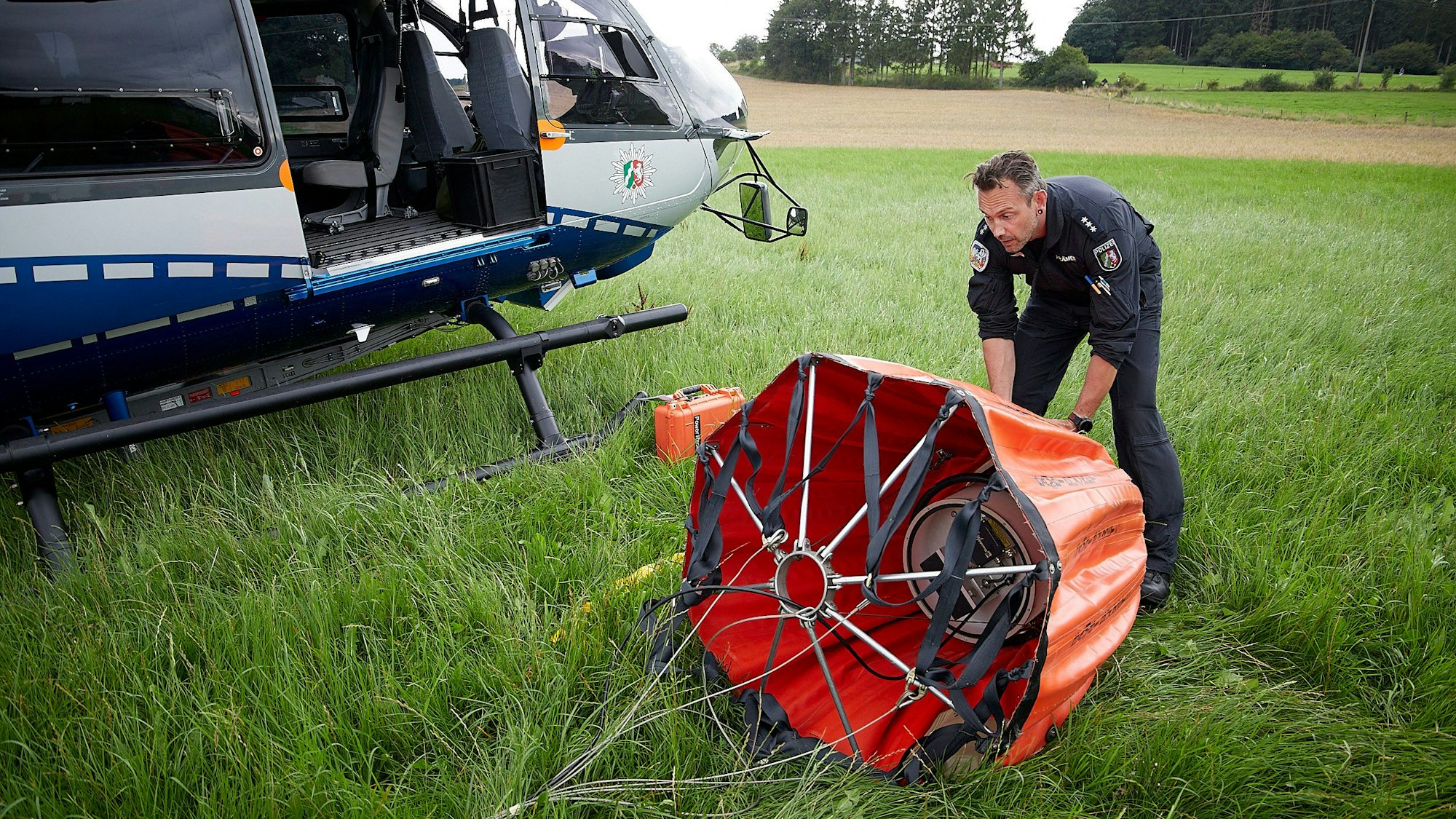Das Bild zeigt einen Beamten, der einen roten Behälter an einem Hubschrauber befestigt.