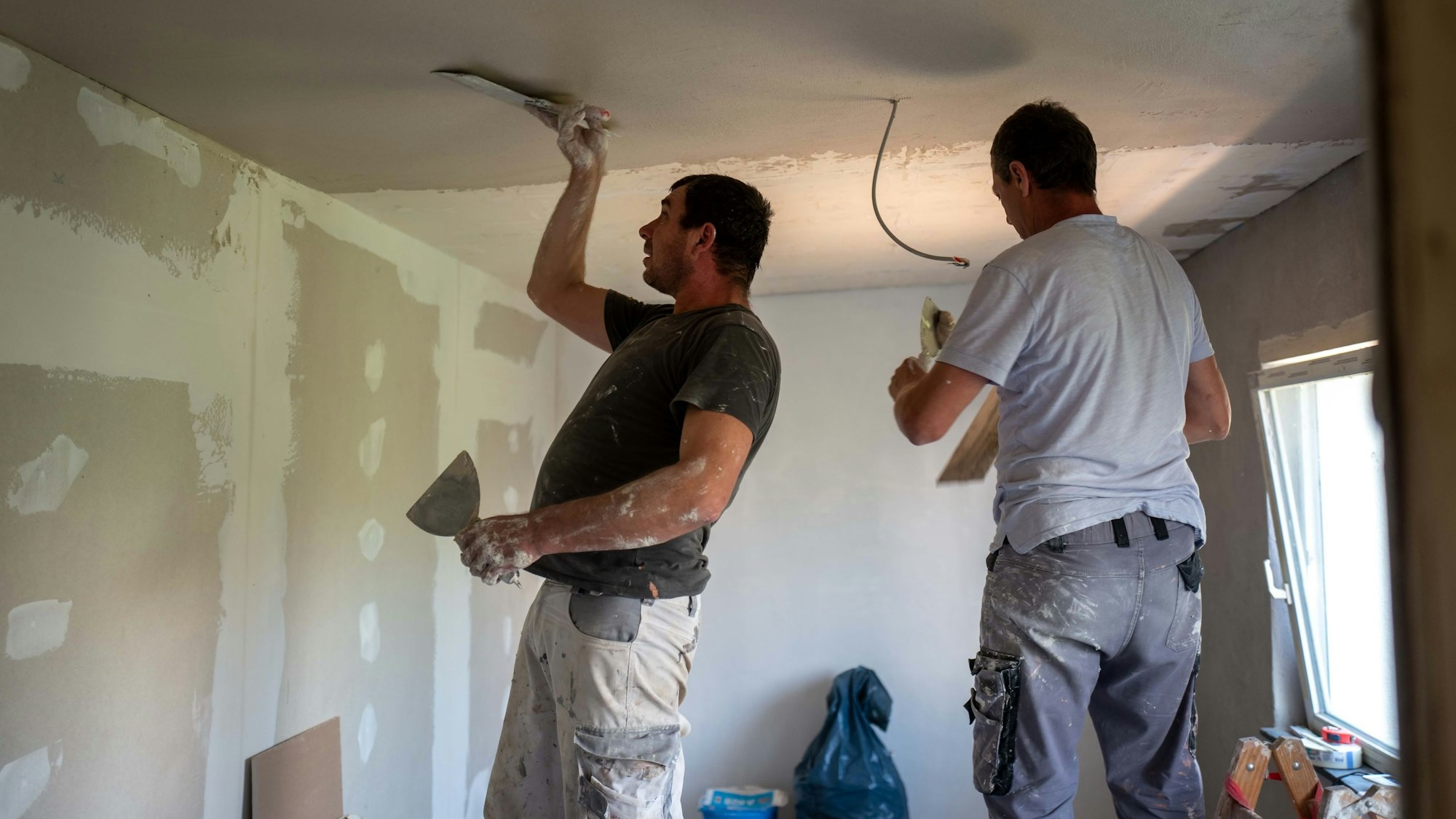 Zwei Arbeiter verputzen die Decke.