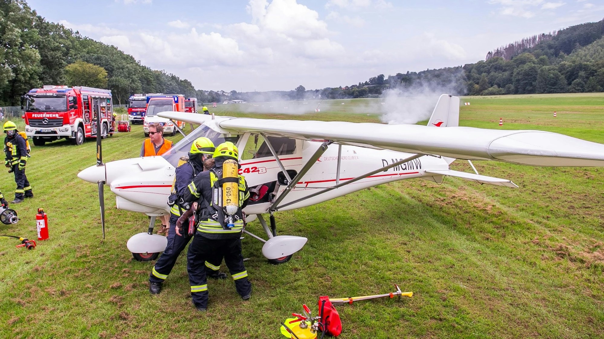 An einem qualmenden Kleinflugzeug stehen Rettungskräfte der Feuerwehr.