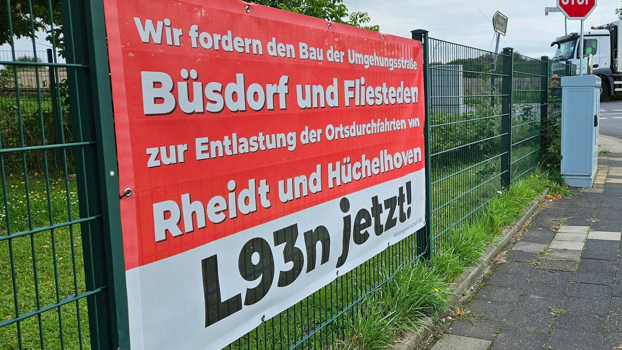 Auf einem Plakat in Rheidt-Hüchelhoven wird der Bau der Ortsumgehung für Pulheim, Fliesteden und Büsdorf, der L93n, gefordert.