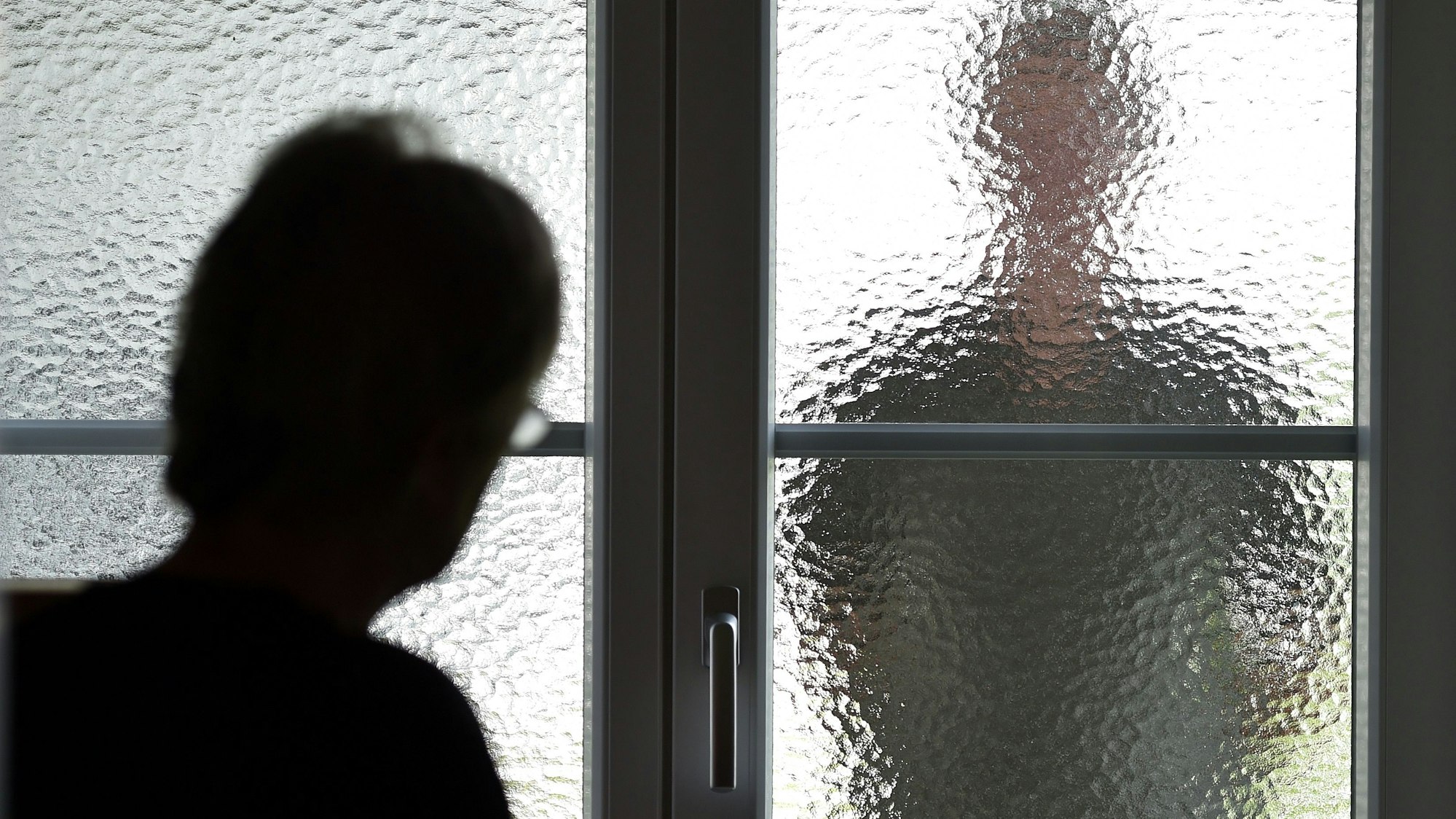 Eine Frau steht an einer Glasscheibe, hinter der ein Stalker steht (gestellte Szene).