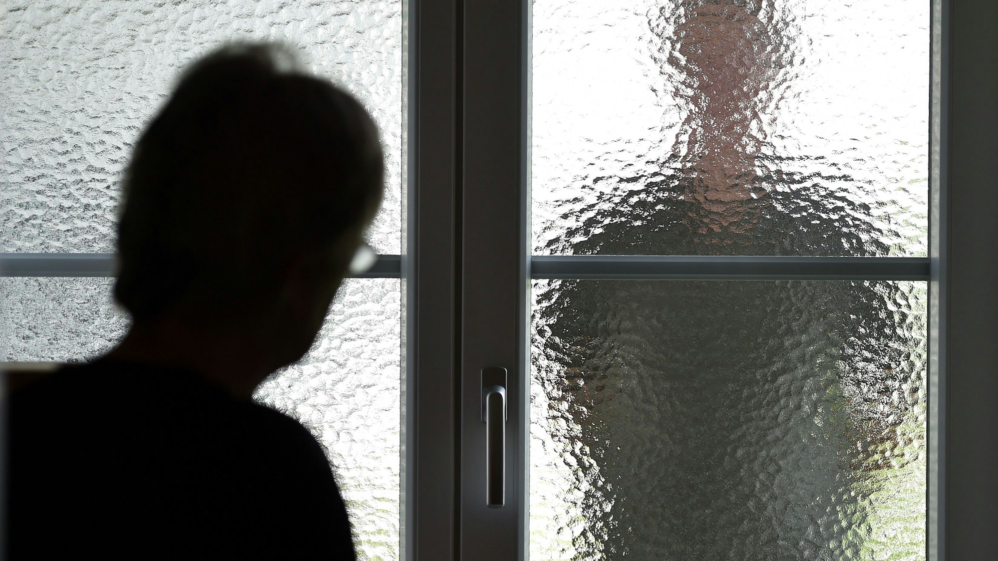 Eine Frau steht an einer Glasscheibe, hinter der ein Stalker steht. (gestellte Szene).