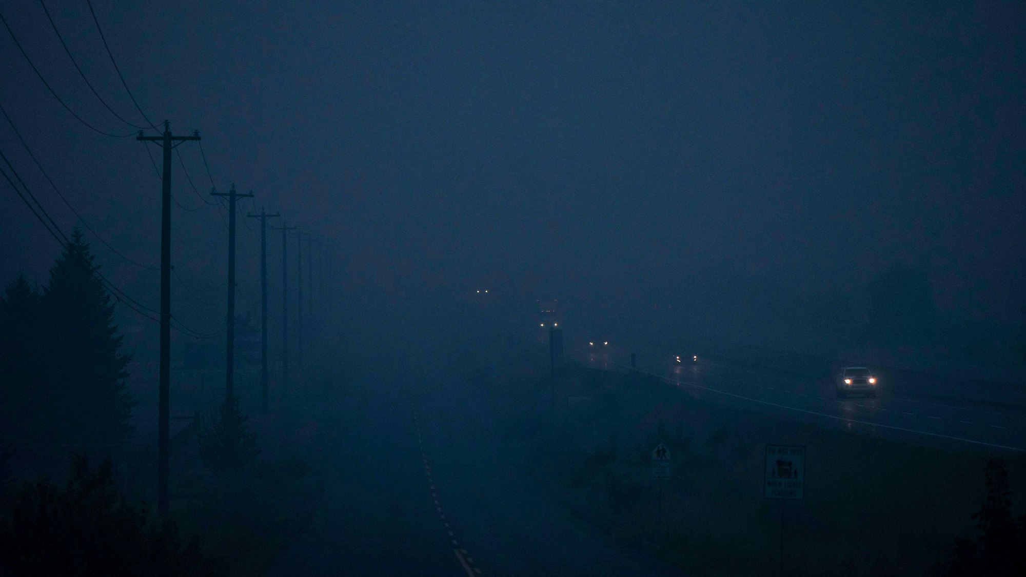 Autos fahren über eine vom Rauch vernebelte Straße, am linken Bildrand sind Silhouetten von Leitungsmasten zu erkennen.