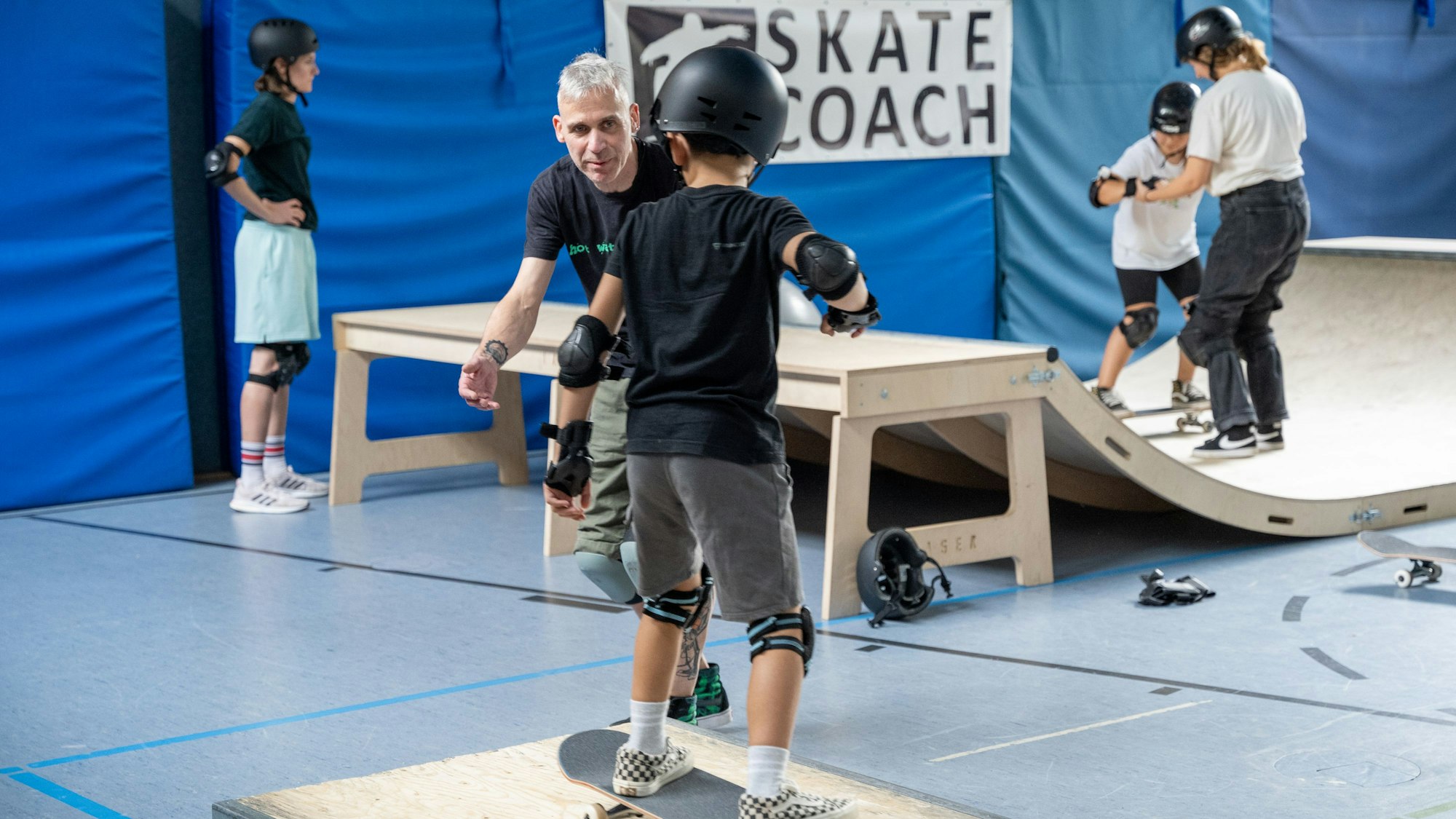 Michael Gorrison hilft einem Kind dabei, über eine Rampe zu skaten.