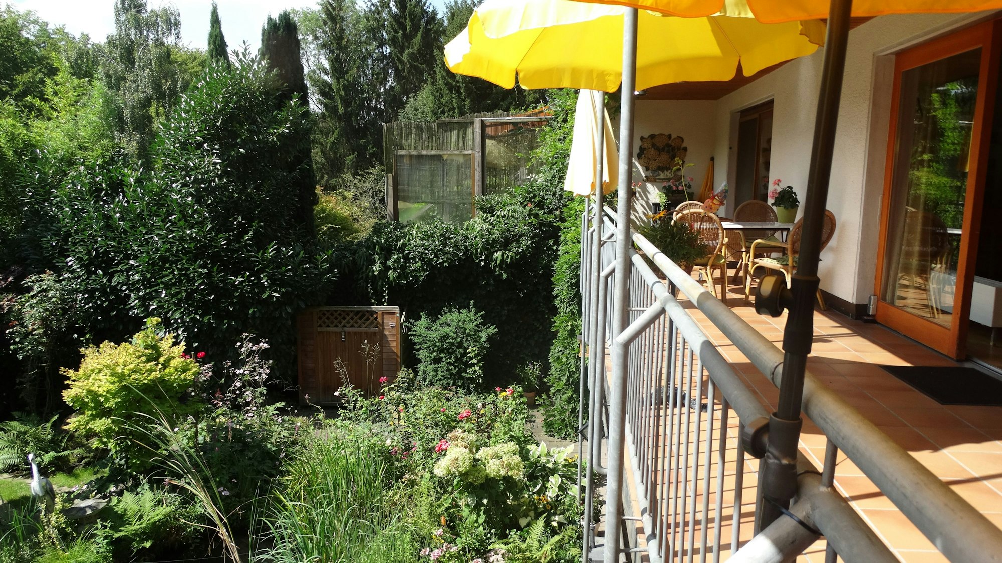 Blick von einem Balkon mit einem gelben Sonnenschirm in den üppig-grünen Garten.