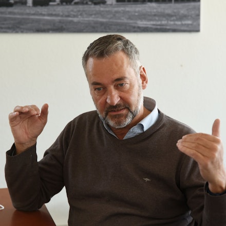 Hein Mulders trägt einen Pulli und darunter ein Hemd. Er hat einen grau melierten Bart und dunkelgraue Haare.