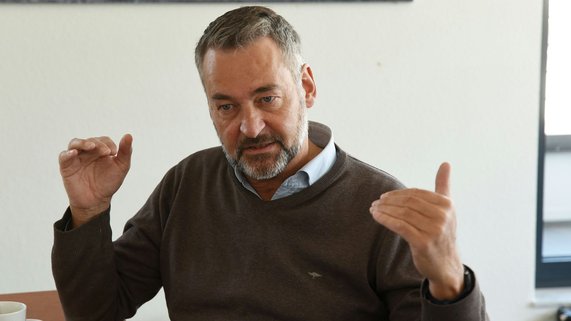 Hein Mulders trägt einen Pulli und darunter ein Hemd. Er hat einen grau melierten Bart und dunkelgraue Haare.