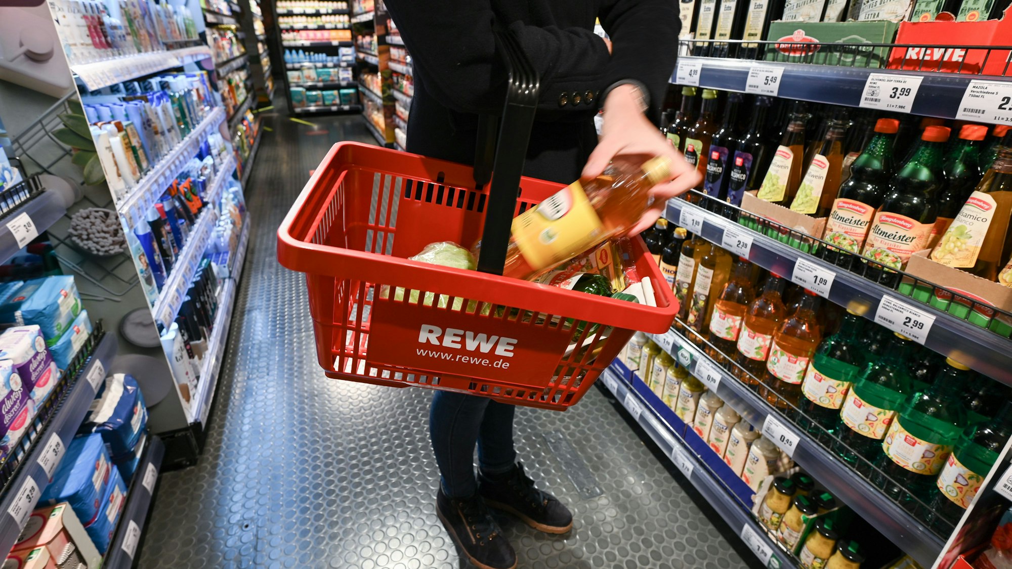 Eine Frau steht im Frankfurter Hauptbahnhof mit einem Einkaufskorb vor einem Lebensmittelregal.