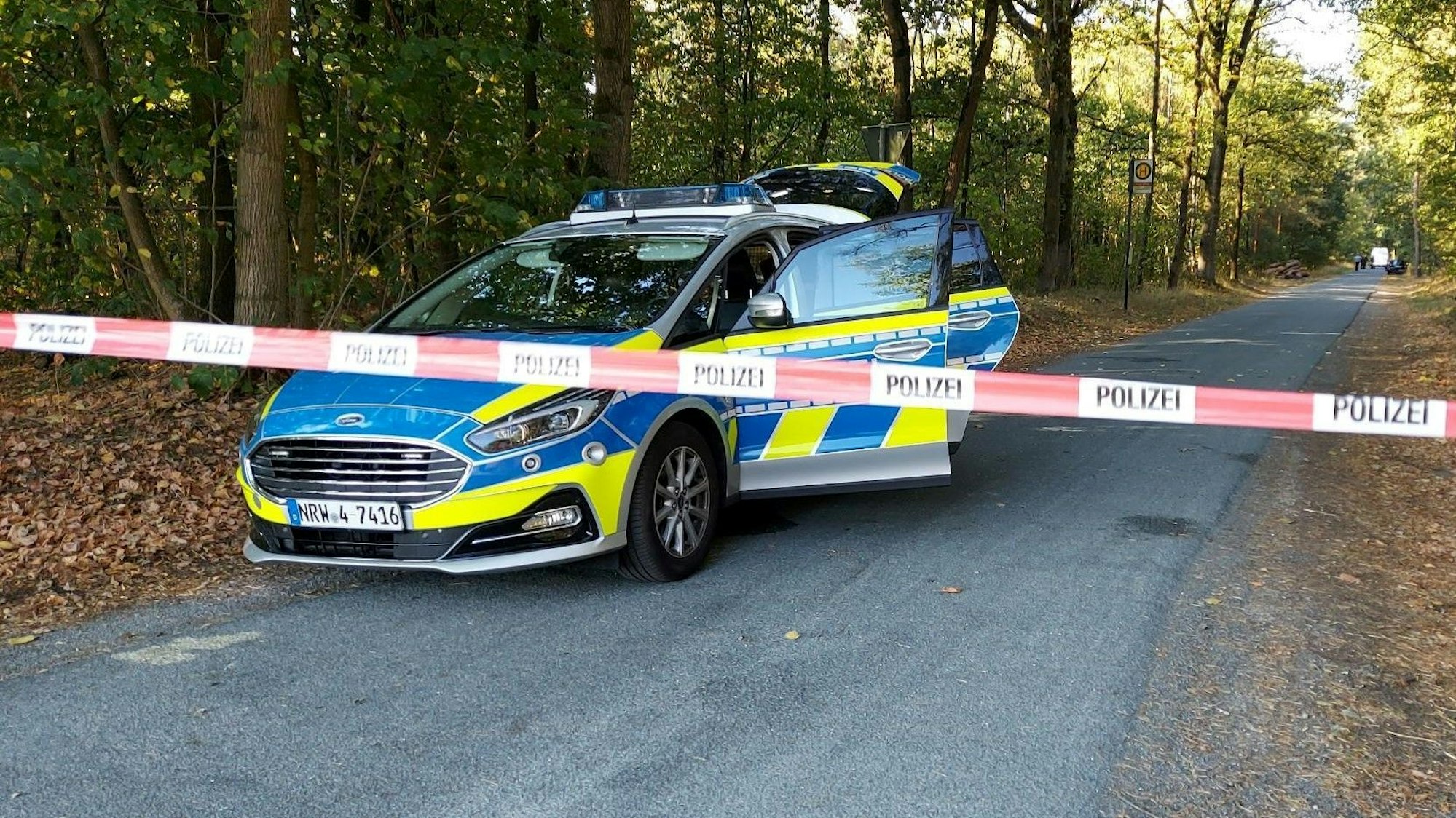 Ein Polizeiauto steht an einem mit Flatterband abgesperrten Waldweg. Bei dem Foto handelt es sich um ein Symbolfoto.