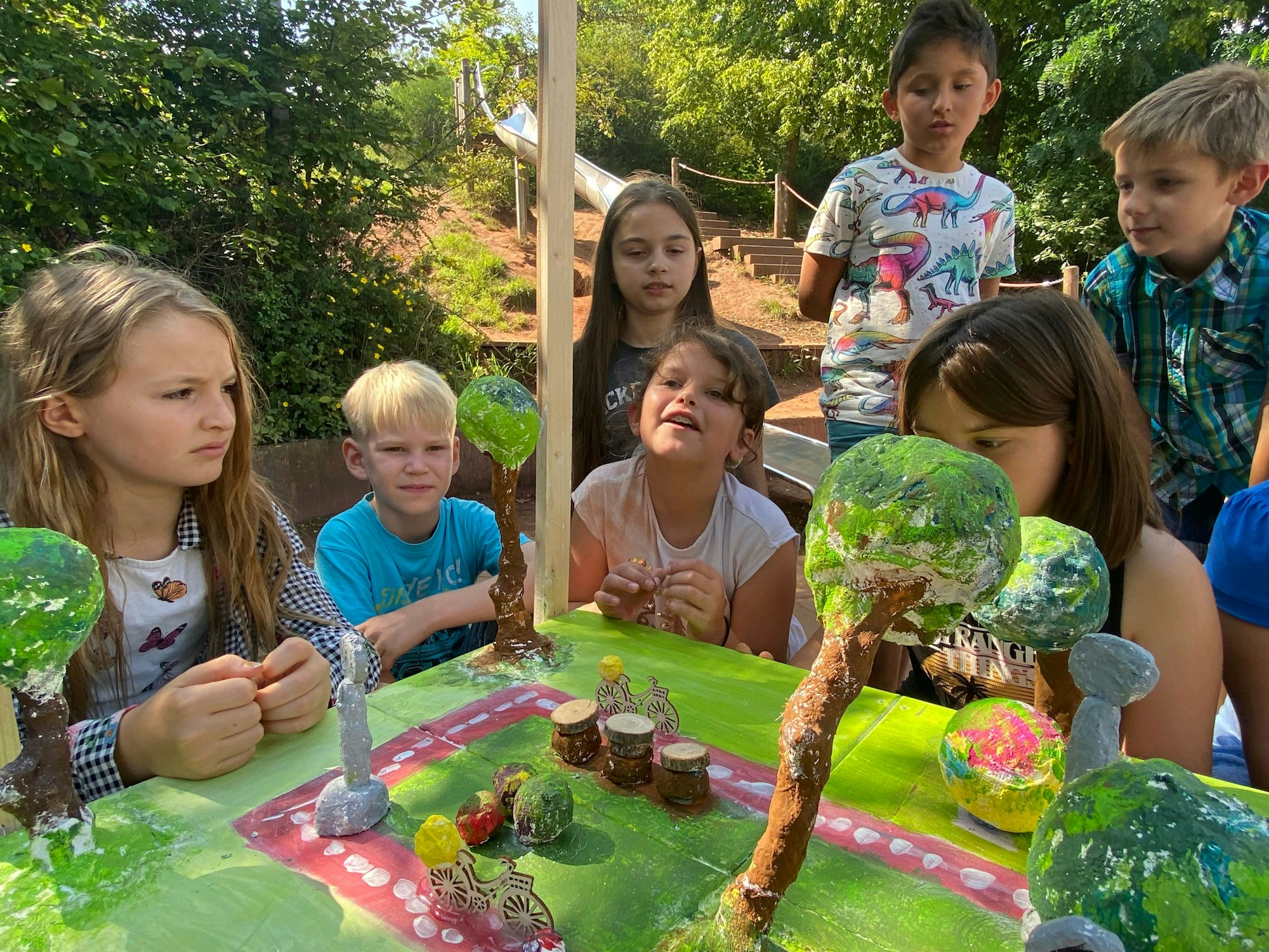 Um ein buntes Modell aus Pappmaché reihen sich Schulkinder. In dem Modell zu sehen sind rote Radwege, Bäume und Fahrräder.