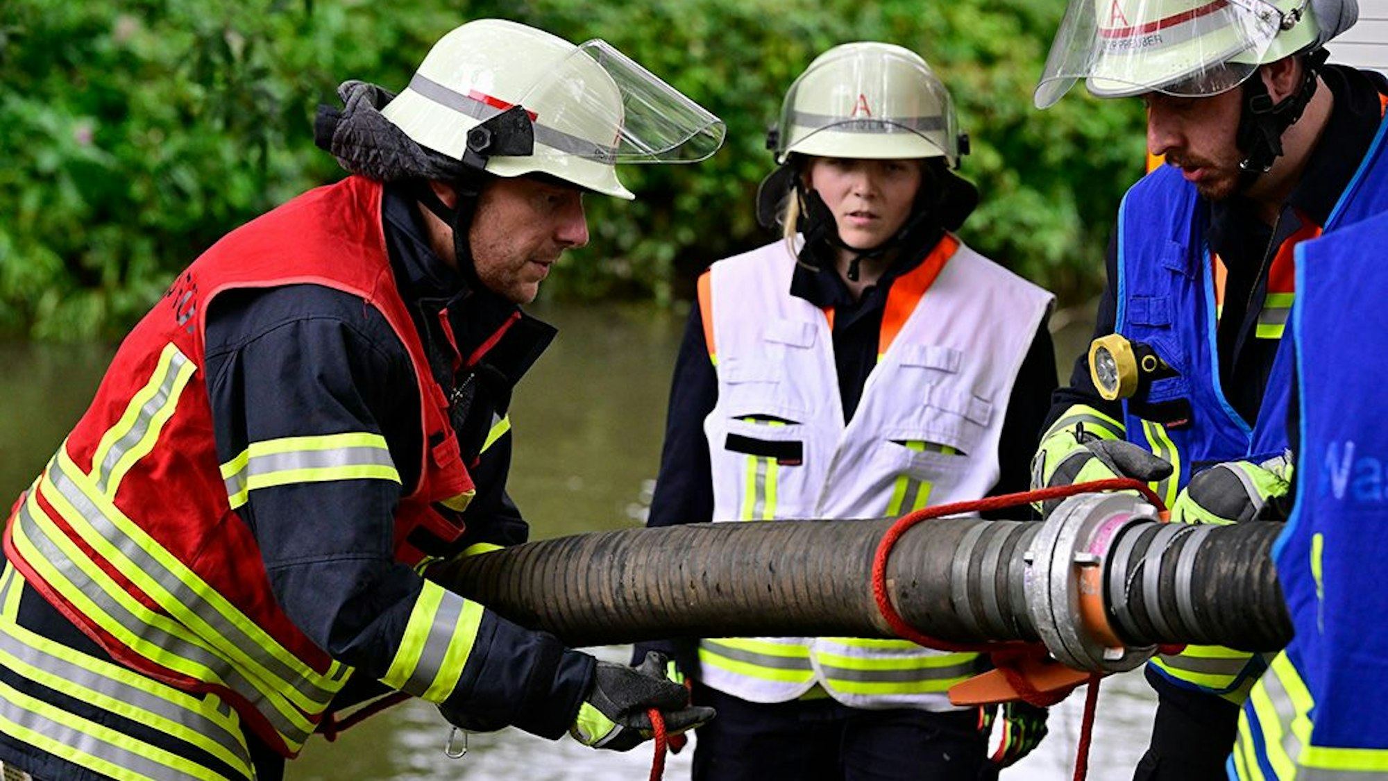 Feuerwehrleutemontieren einen Saugschlauch, um Löschwasser aus einem Fluss im Hintergrund zu fördern.