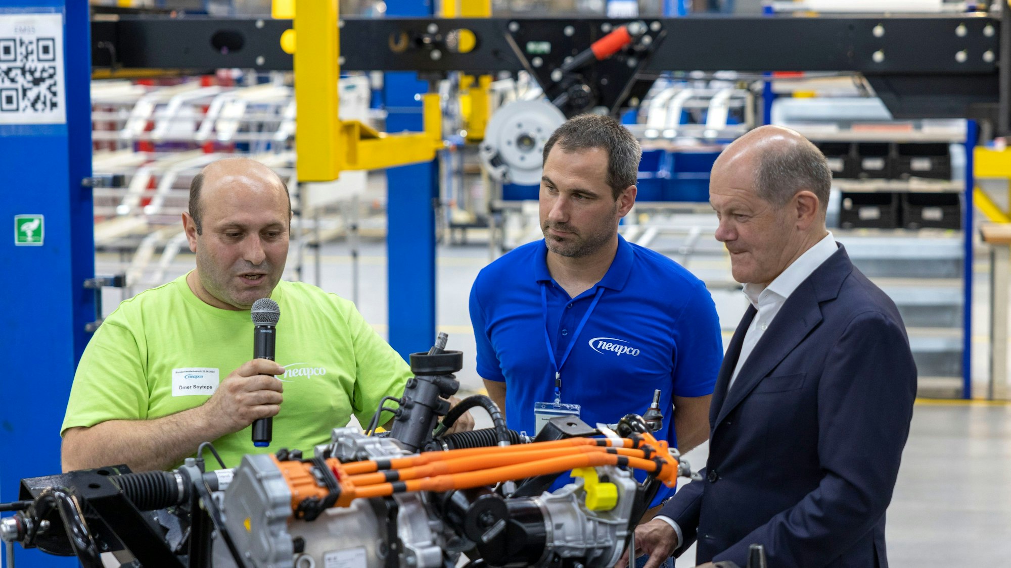 Düren: Bundeskanzler Olaf Scholz (SPD, r) lässt sich von Mitarbeitern während seines Besuchs im Werk der Neapco Europe GmbH (Automobilzulieferer) in Düren die Montage eines Elektromotors erklären.