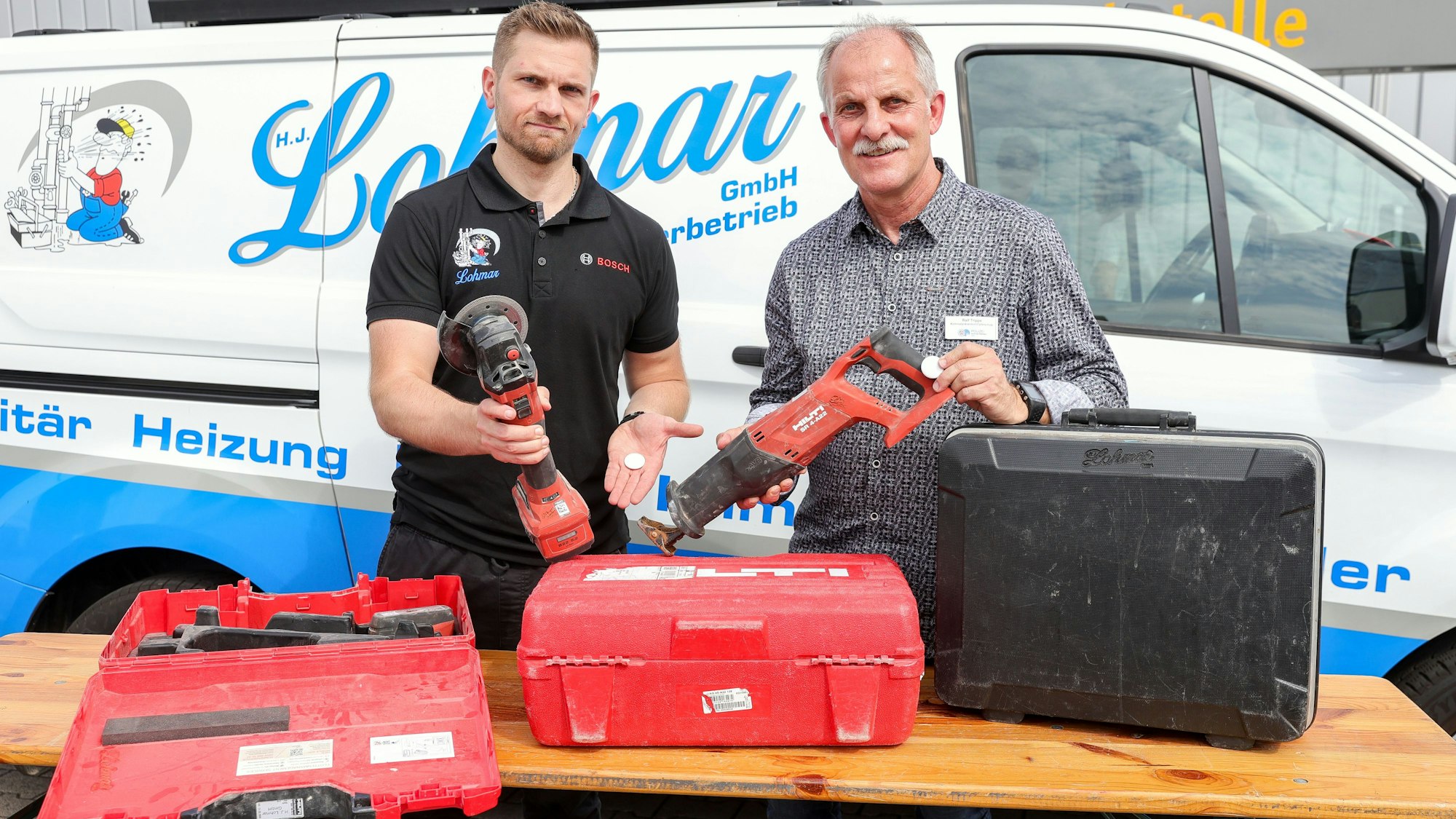 Patrick Lohmar, Inhaber der Sanitärfirma Lohmar, und Ralf Trippe von der Polizei Köln stehen vor einem Kleintransporter der Firma und halten Werkzeuge in der Hand.
