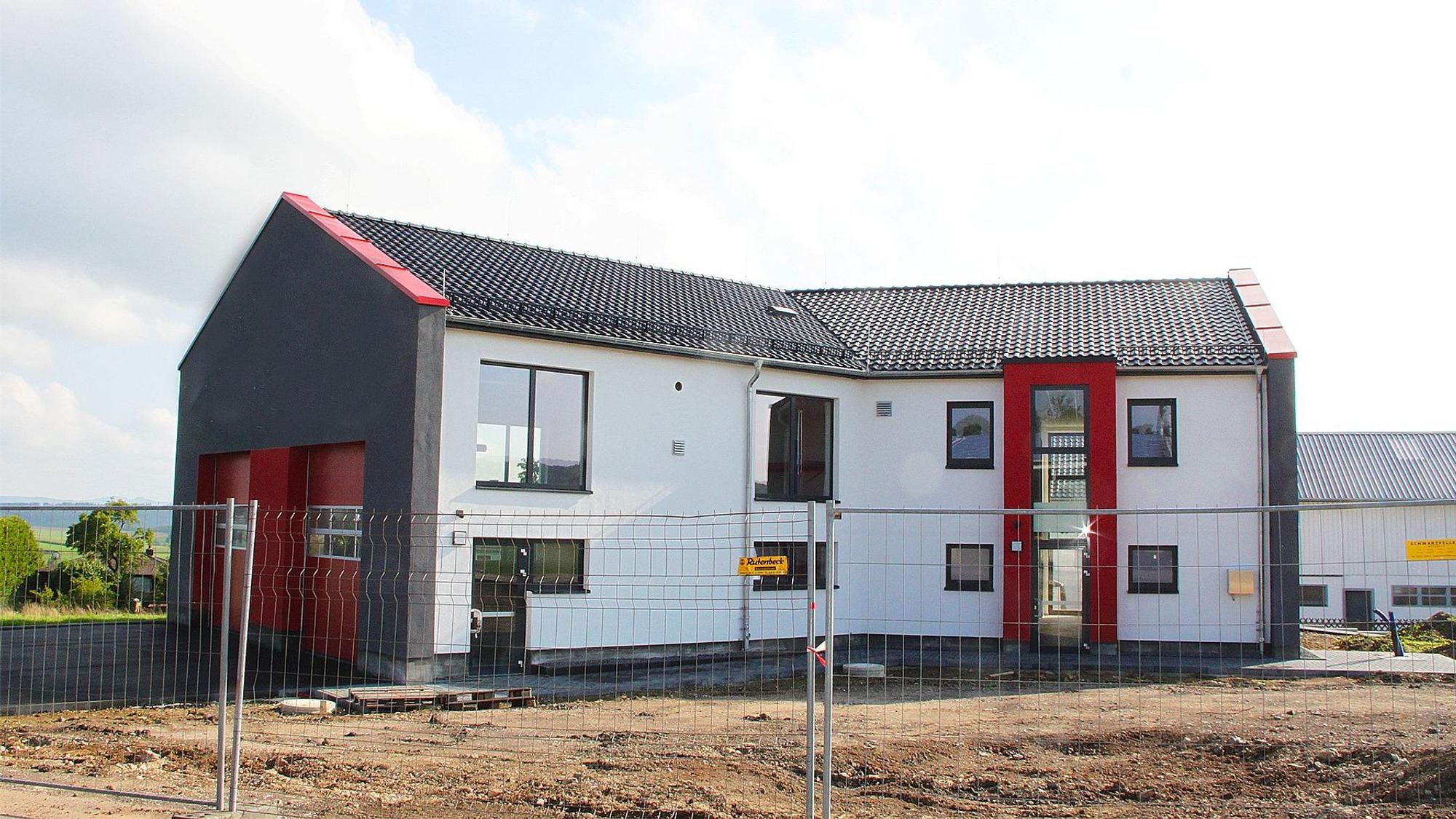 Das neue Feuerwehrgerätehaus mit der weißen Fassade und den roten Toren ist fast bezugsfertig. Noch steht jedoch ein Bauzaun davor.
