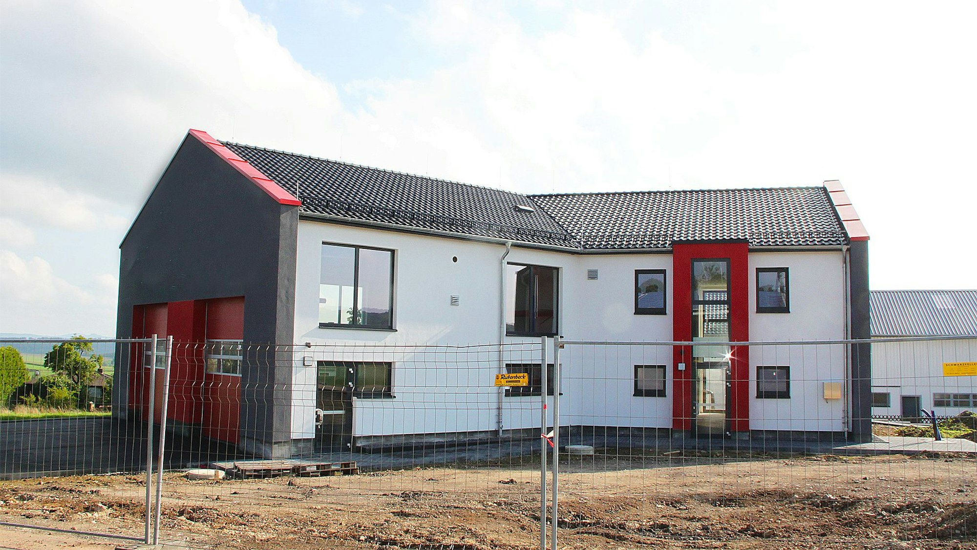Das neue Feuerwehrgerätehaus mit der weißen Fassade und den roten Toren ist fast bezugsfertig. Noch steht jedoch ein Bauzaun davor.