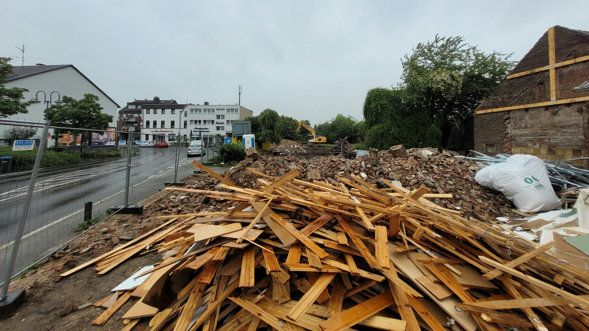 Auf einem Grundstück an einer Straße, das durch einen Bauzaun abgegrenzt ist,  liegt Schutt und Holz.