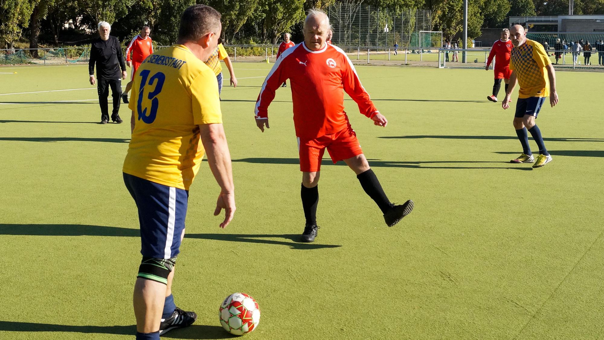 Fußballer in gelben und roten Trikots spielen Walking Football gegeneinander.