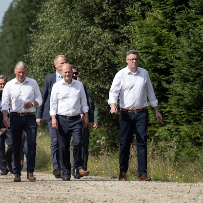Spaziergang im Windpark:  Bundeskanzler Olaf Scholz (SPD, 2.v.r.) und Hendrik Wüst (2.v.l.), Ministerpräsident von Nordrhein-Westfalen, und Bernd Goffart, Bürgermeister (M., beide CDU) sind bei ihrer Tour in der Eifel zu sehen.