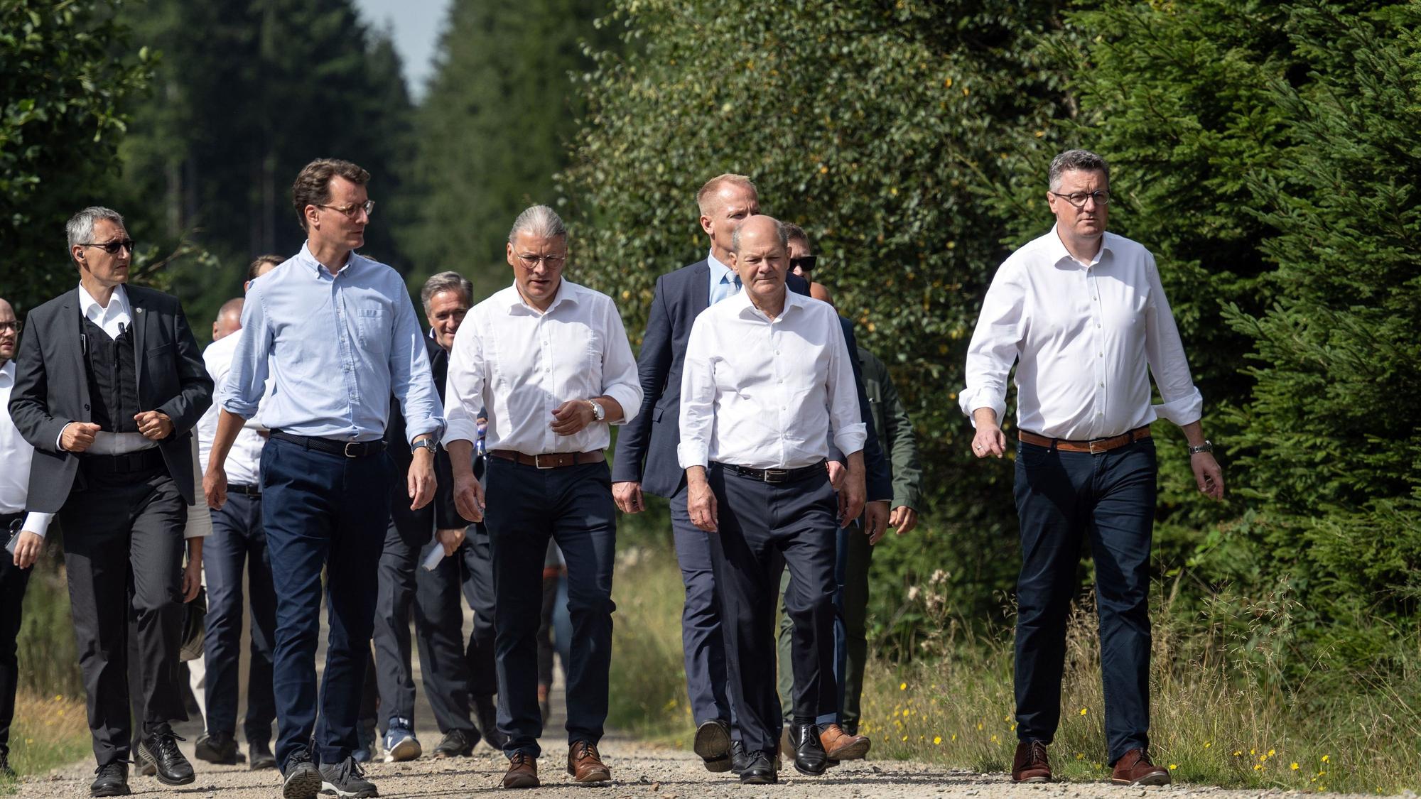 Spaziergang im Windpark: Bundeskanzler Olaf Scholz (SPD, 2.v.r.) und Hendrik Wüst (2.v.l.), Ministerpräsident von Nordrhein-Westfalen, und Bernd Goffart, Bürgermeister (M., beide CDU) sind bei ihrer Tour in der Eifel zu sehen.
