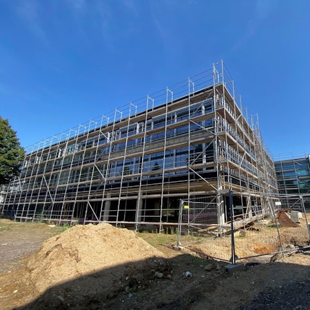 Das Bild zeigt den dreigeschossigen Neubau der Schule, der noch von einem Gerüst umgeben ist.