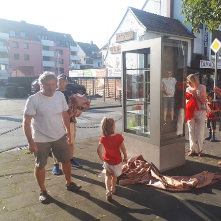 Auf dem Bürgersteig an einer kleinen Straße steht ein nagelneuer Schrank mit Glasscheiben und Glasböden für Bücher.