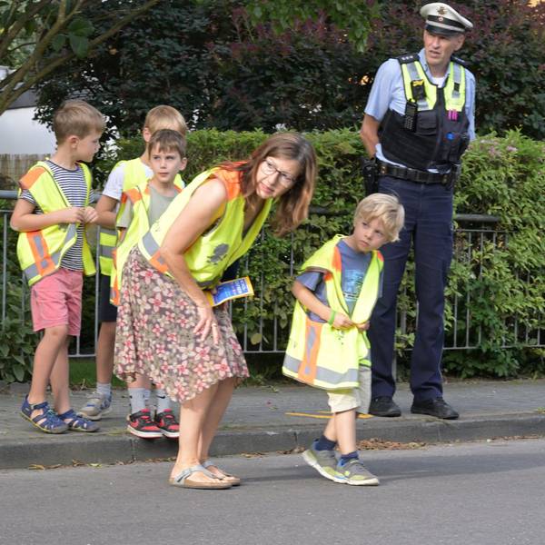 Eine Lehrerin und ein Polizist helfen Grundschülern über die Straße.