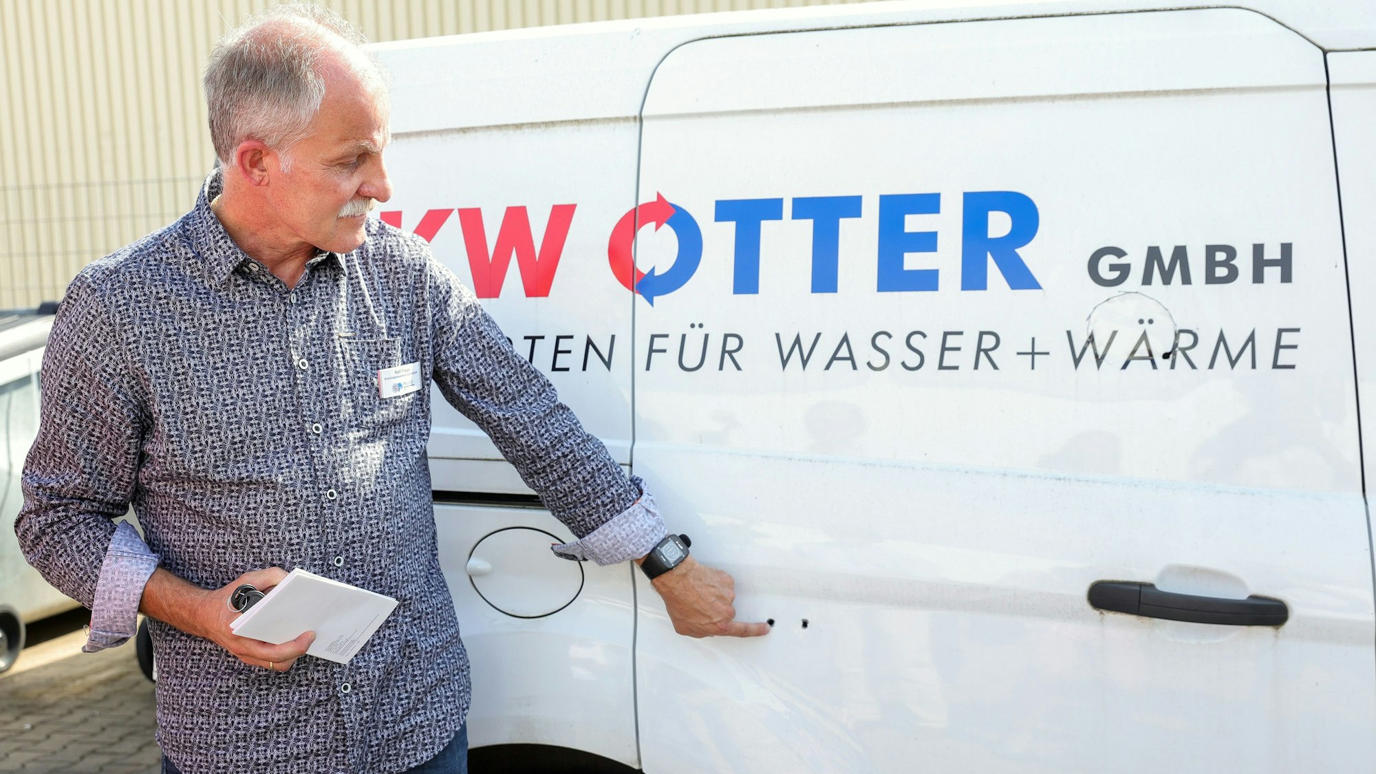 Ralf Trippe von der Polizei Köln zeigt zwei Bohrlöcher in einer Seitentür eines Handwerkerautos, über die die Täter die Schiebetür aufgebrochen haben.